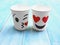 Two white paper cups with face kiss and smile on wood table.