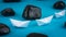 Two White Paper Ships in Sigle File between Abstract Black Rock Stones on Blue Background