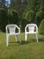 Two white plastic chairs stand on the lawn