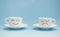 Two white porcelain cups, saucer, with a cheerful and sad emotion on a blue background. Vigorous, and sleepy mood. Copy spase
