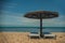 two white sun loungers under a wooden beach umbrella on a rocky beach in summer on a clear day without people