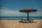 two white sun loungers under a wooden beach umbrella on a rocky beach in summer on a clear day without people