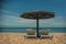 two white sun loungers under a wooden beach umbrella on a rocky beach in summer on a clear day without people