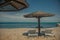 two white sun loungers under a wooden beach umbrella on a rocky beach in summer on a clear day without people