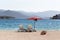 Two white sunbeds standing on a pebble beach with a red parasol in the background of the blue sea and mountains