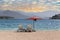 Two white sunbeds standing on a pebble beach with a red parasol in the background of the blue sea and mountains