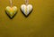 Two white and yellow metal hearts on a golden paper background