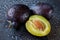 Two whole and one half sliced Damson plums with the stone on a black cutting board with water drops. Macro shot of fresh, organic