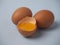 Two whole raw brown chicken eggs and a broken half egg with yellow yolk closeup on a blue background