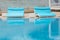 Two wide turquoise deck chairs are beside the pool, reflected in the water, concept travel, vacation