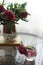 Two wilted bouquet of peonies flowers in a vase and a jar on a glass table.