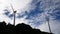 Two windmills spinning in the background of blue sky with clouds