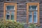 Two windows in a wooden house of the early 20th century with mustard trim and antique frames with patterns