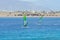 Two windsurfers on a board under a sail move on the sea, against a background of a sandy coast, mountains,