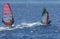 Two windsurfers on sailboards are moving at a speed along the sea surface