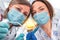 Two woman dentists in medical masks standing right above the patient, holding tools and ready to start working, dentistry and