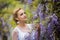 Two woman hands holding wisteria blooming vineA portrait of young Caucasian woman with blond hair near purple wisteria, looking up