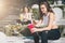 Two women athletes in sports clothes are sitting on bench, relax after sports training, use smartphones, listen to music