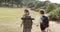 Two women with backpacks hike in a grassy outdoor setting