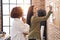 Two women business workers writing on cork board at office