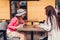 Two women chatting while having coffe in outdoor cafe. Happy friends using phone checking pictures. Girls hang out