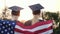 Two women college graduates with America flag on shoulders, rear view