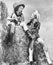 Two women in cowboy hats sitting on a haystack