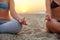 Two women doing group meditation on the beach on sunrise. Female friends doing yoga padmasana or lotus asana sitting on