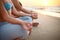 Two women doing group meditation on the beach on sunrise. Female friends doing yoga padmasana or lotus asana sitting on