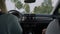 Two women driving car on narrow road with deciduous trees on both sides approaching to small European town. Back view