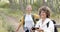 Two women enjoy a hike in a wooded area, one with a phone in hand
