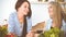 Two women friends choosing the recipe for a delicious meal while sitting at the table in the kitchen. Tablet pc is the