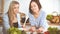 Two women friends choosing the recipe for a delicious meal while sitting at the table in the kitchen. Tablet pc is the