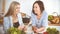 Two women friends choosing the recipe for a delicious meal while sitting at the table in the kitchen. Tablet pc is the