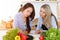 Two women friends choosing the recipe for a delicious meal while sitting at the table in sunny kitchen. Tablet pc is the