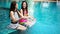 Two women friends splashing water in swimming pool