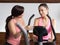 Two women gym instructor talking listening bike sitting standing