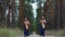 Two women harpists walk at forest and play harps on background of pines.