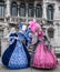 Two women holding fans and wearing hand painted masks and ornate blue and pink costumes at Venice Carnival