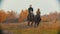 Two women on the horses backs running on the autumn field - a dog following them