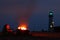 Two women keep a fire going within sight of a lighthouse