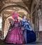 Two women in masks and ornate blue and pink costumes standing under the arches in the Railto Market, Venice during carnival