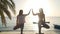 Two women practice tree yoga posture and given the five to each other at sunset