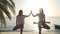 Two women practice tree yoga posture and given the five to each other at sunset