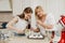 Two women are putting a whipped meringue on a tray with a spoon and a scapula