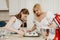 Two women are putting a whipped meringue on a tray with a spoon and a scapula