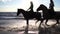 Two women ride on horse at river beach in water sunset light