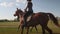 Two women are riding horses along a field