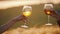 Two women`s hands clink glasses on a background of sunset ears of rye. Cheers