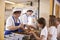 Two women serving food to a girl in a school cafeteria queue